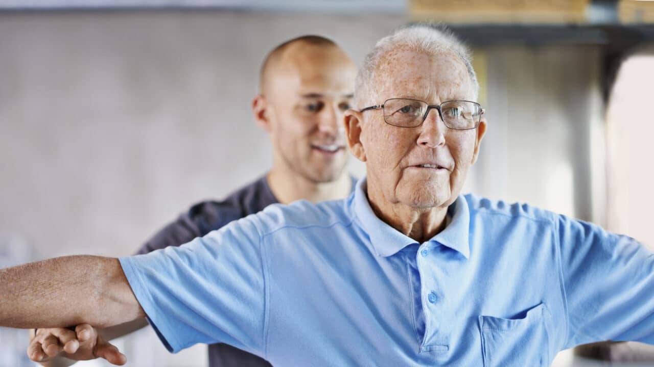 Fysioterapeutti auttaa iäkästä miestä venyttelemään.