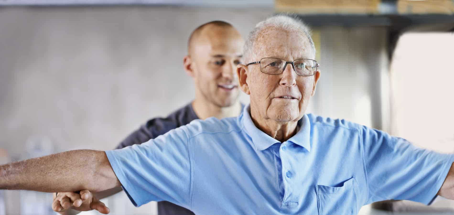 Fysioterapeutti auttaa iäkästä miestä venyttelemään.