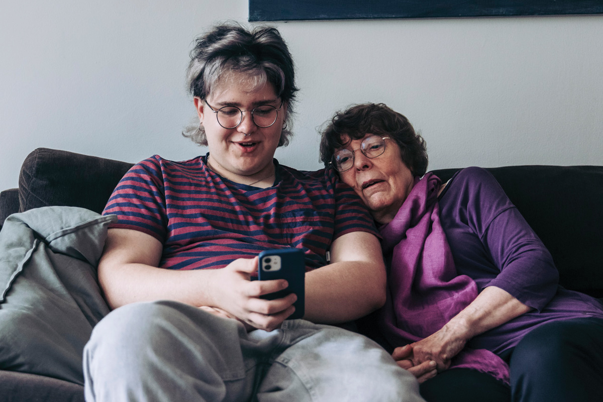 Tonårig pojke på soffan med äldre kvinna tittar på telefonen tillsammans