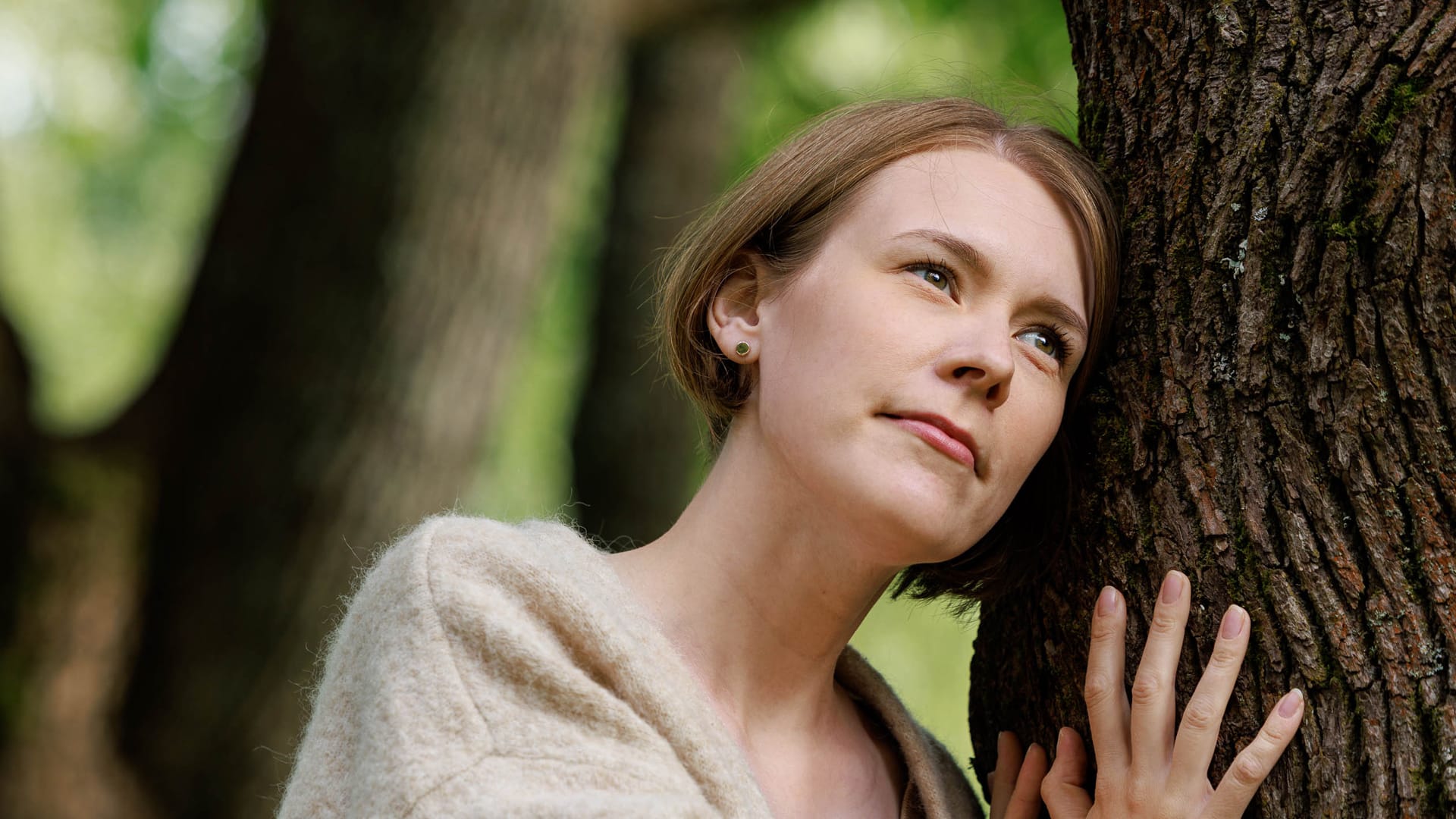 Närbild av kvinna som lutar huvudet mot en trädstam.